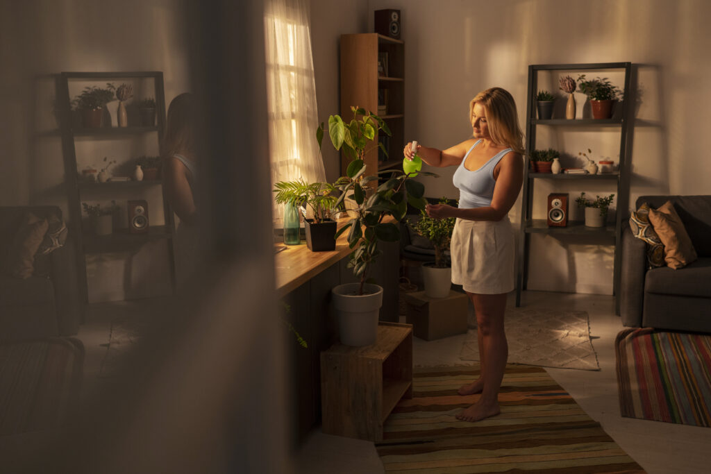 Woman misting indoor plants in a sunlit living room styled with layered rugs, wooden furniture, and potted greenery—an effortless aesthetic room ideas vibe.